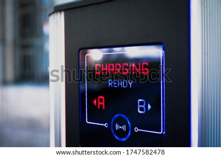 Electric car charging station in city parking with active Charging sign in red