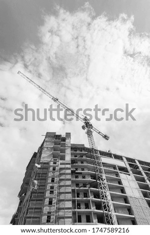 Black and white photo of a multi-storey residential building under construction and crane on a background of blue sky