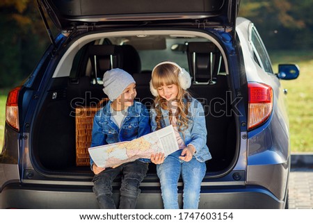 Agreeable little boy and girl are looking at the road map while sitting in the auto's trunk and discussing the move direction. Family vacation trip by car. Royalty-Free Stock Photo #1747603154