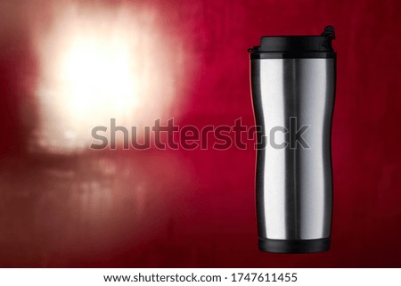 stainless steel coffee cup front view. thermal travel mug to drink hot beverage tea. on a red colored blurred background. blank for design. studio shot.