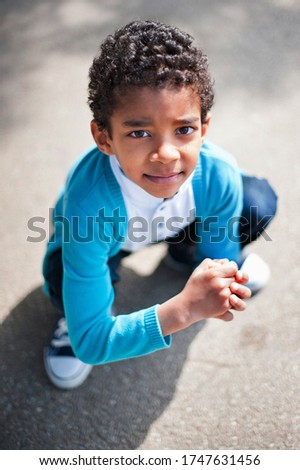 Little cute real black boy siting down in the park in summertime.