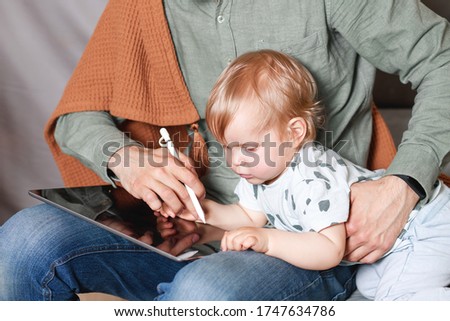 A young man works at home with a tablet computer and a baby in his arms. The stay at home concept. Home office with children.