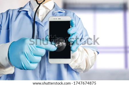 Photo of a doctor in uniform with stethoscope holding a smartphone and listening to it.