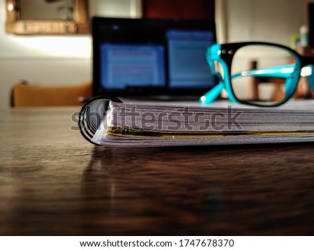 Eyeglasses on a notebook with computer behind on the brown table