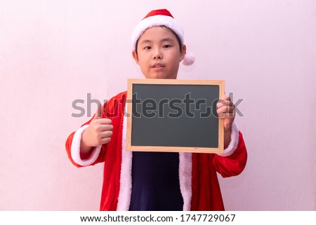 Asian boy in Santa Claus clothes holding empty board. Merry christmas