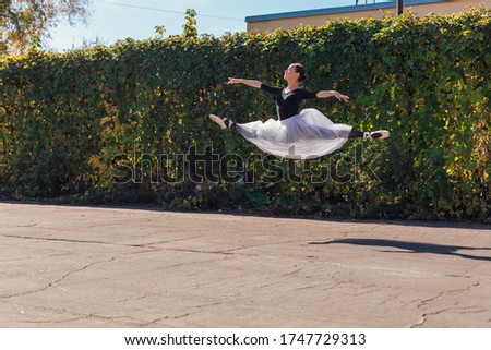 Woman ballerina in a white ballet skirt dancing in pointe shoes in a golden autumn park. Ballerina jumping doing a split