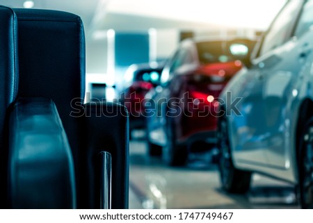Blurred new luxury red and gray car parked in modern showroom. Selective focus on black leather sofa in modern showroom. Car dealership. Showroom interior. Automotive industry on coronavirus crisis.