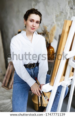  Female artist sitting on chair in front of easel, painting a picture on a background of Gypsum  heads.Сreativity, hobby, job and creative occupation concept.Artist 