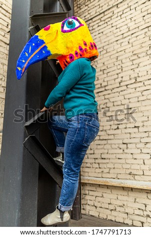 Masked woman - brightly colored bird head with a large beak climbing at metal construction. homemade original costume for the holiday.