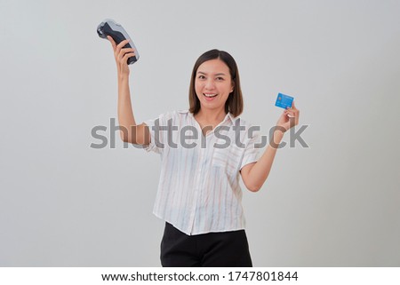 Young smiling beautiful asian woman presenting credit card in hand showing and wireless modern bank payment terminal for making payment