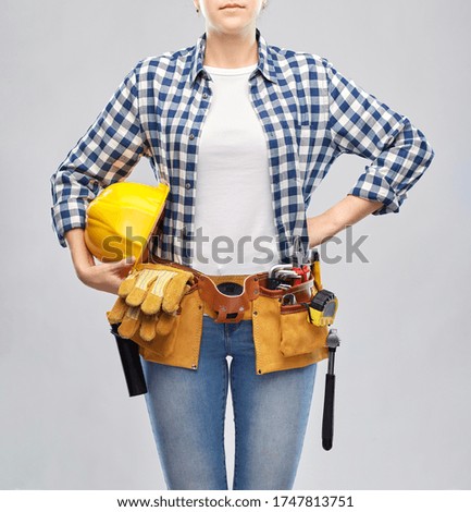 repair, construction and building concept - woman or builder with helmet and working tools on belt over grey background