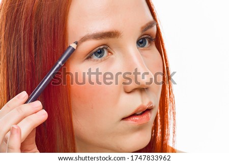 a close beauty portrait of a red-haired girl who has clean skin and uses an eyebrow pencil. Isolated on a white background.