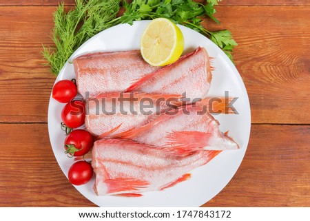 Raw headless gutted carcasses of redfish also known as ocean perch on the dish with lemon and cherry tomatoes on the rustic table, top view  Royalty-Free Stock Photo #1747843172