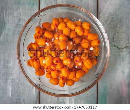 Frozen sea buckthorn berries in a deep glass plate on a wooden background