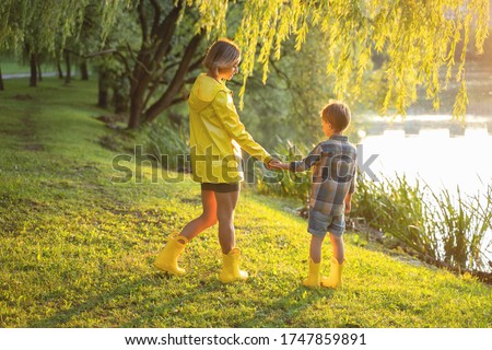 Beautiful young mother with little son walking in the park after a rain.