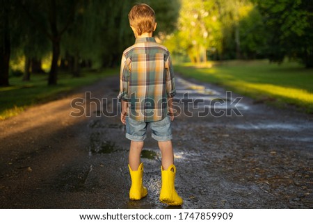 Preschooler child wearing yellow rain boots walking in park after rain. Kid playing and having fun in sunny spring or summer day. Outdoors games for children