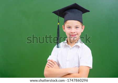 Boy on the background of a green blackboard in a graduation cap