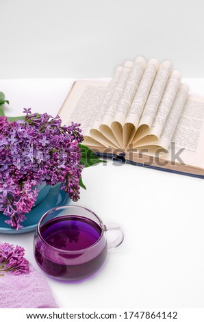 A cup of fragrant purple Clitoria tea and a bouquet of lilac in a blue cup, an open book on a white background. Selective focus, romantic concept, verti?al background, copy space