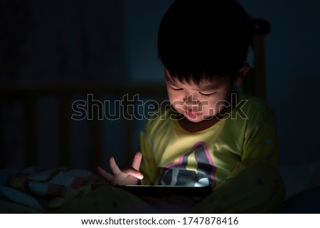 Eye close up Little boy are watching video in tablet on bed at night time light flashes reflected from the screen,children using games with addiction and cartoon concepts