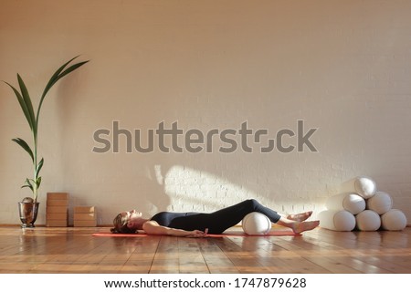 Young woman in corpse pose with knees resting on bolster doing breathing exercise at yoga session at home during self-isolation during corona virus Royalty-Free Stock Photo #1747879628