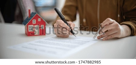 Cropped shot of A woman signing home loan agreement while holding house key on white table with hose model 