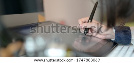 Close up view of female graphic designer working on drawing tablet with stylus pen on office desk 