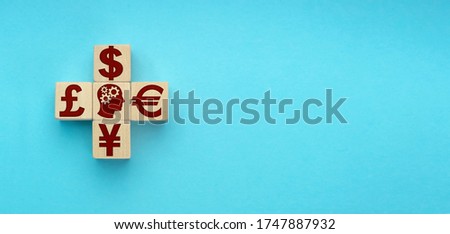 wooden blocks in the form of a cross with currency symbols of the world on blue background.