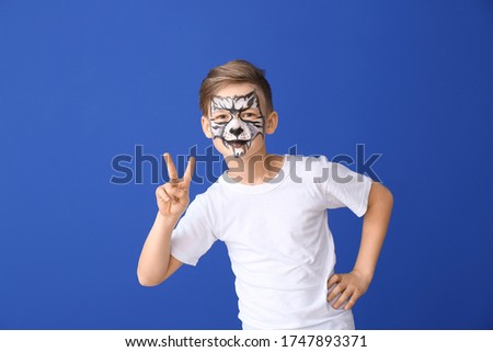 Funny little boy with face painting on color background