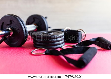 Fitness equipment, green dumbbells and a rubber expander with black handles on a pink background, space for text
