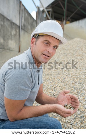 builder holding pebbles outside factory