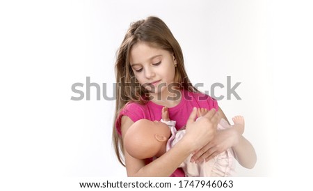 Girl on a white background holds a doll in her hands and plays with the doll. Children's games with toys.