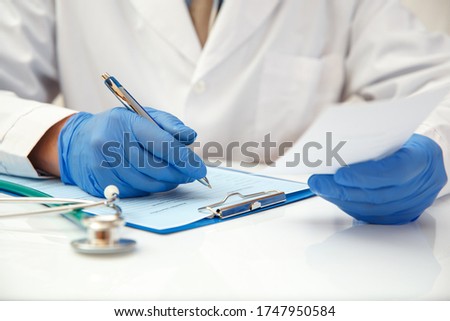 A doctor in protective gloves writes out a prescription for medicines.