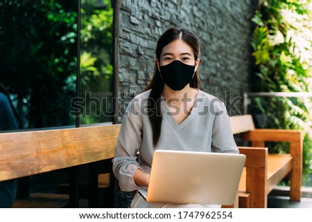 Asian woman wearing a face mask outside while sitting on laptop. Don't forget to wear a mask and face mask requirement to go outside concept.
