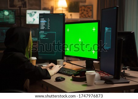 Female hacker wearing a hoodie in front of computer with green screen.