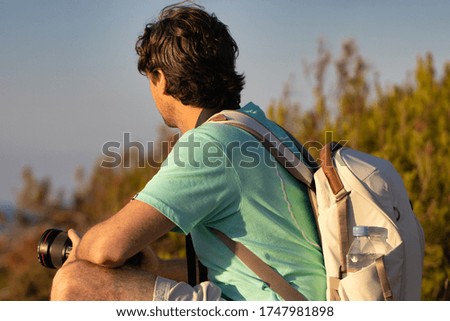 Young Man Taking Pictures of a Mountain Landscape Travel Photographer is taking photos with camera of hills landscape at sunset, Lens Flare. man sitting outdoors