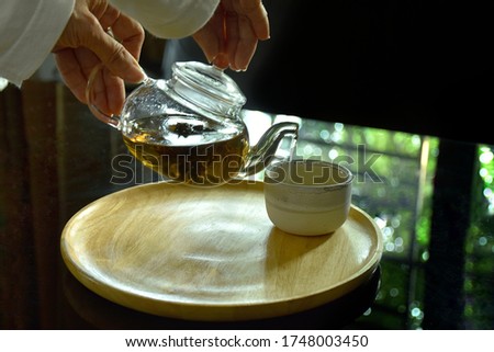 Blur picture of hot tea from tea leaves in glass teapot with ceramic cup on wood place with selective focus on, use for advertising work