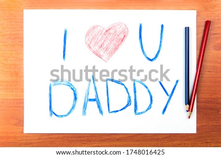 Fathers day concept. Composition with childs drawing with words I Love U Daddy and red heart, and color pencils on wooden desk.