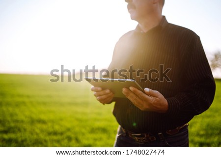 Farmer on a green wheat field with a tablet in his hands. Smart farm. Farmer checking his crops on an agricultural field. Ripening ears of wheat field. The concept of the agricultural business.