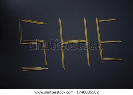 Word 'SHE' written with spaghetti on gray background, top view, copy space. Food supplies, food donation on quarantine while coronavirus.