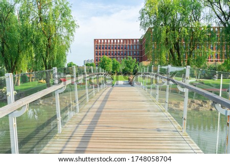 The wood bridge with the glass guardrail. There are some willow trees on the riverside.