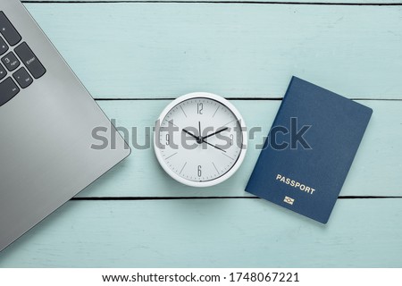 Time to travel. Passport and clock, laptop on blue wooden background. Top view. Flat lay