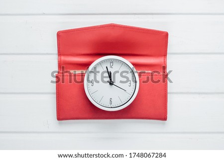 Time to make money. White clock and red wallet on white wooden background. Minimalistic studio shot. Top view