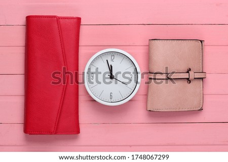 Time to make money. White clock and wallets on pink wooden background. Minimalistic studio shot. Top view