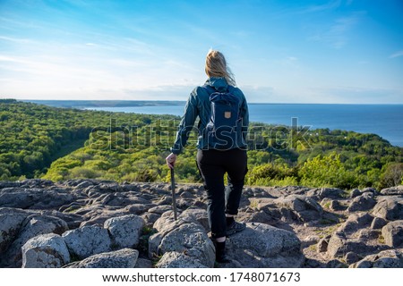 Caucasian Outdoor Active Woman expressing happiness on top of mountain peak at Stenshuvud National Park Overlooking Lush forests with High Biodiversity in Osterlen Skane, South Sweden.  Royalty-Free Stock Photo #1748071673