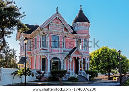 Beautiful pink and white traditional Victorian house. A garden of flowers, lawn and trees. In the background is a beautiful, cloudless, baby blue sky. Royalty-Free Stock Photo #1748076230