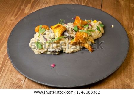 Risotto with wild mushrooms. On a black plate. On a rustic wooden background