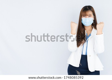 Smiling Asian business woman wearing a medical face mask showing fist fighting over grey background. Back to the normal concept.