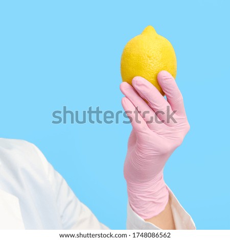 Hand in a medical glove with a yellow lemon on a blue background, close-up.