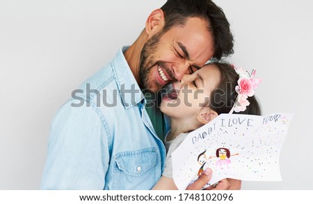 Portrait of a happy daughter giving a drawing greeting card for his happy handsome father on Father's day. Loving daddy and his little girl enjoying time together. Fatherhood and childhood concept.