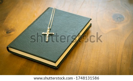 The Cross with the Rosary in the Holy Bible The book is closed, closed with a black cover and Christian symbol on a wooden background.